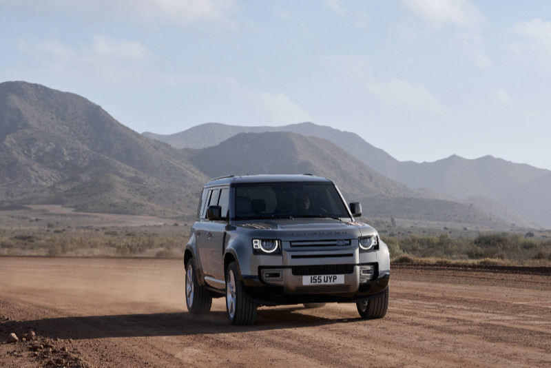 Silberner Defender 110 auf einer Schotterpiste vor Bergkulisse