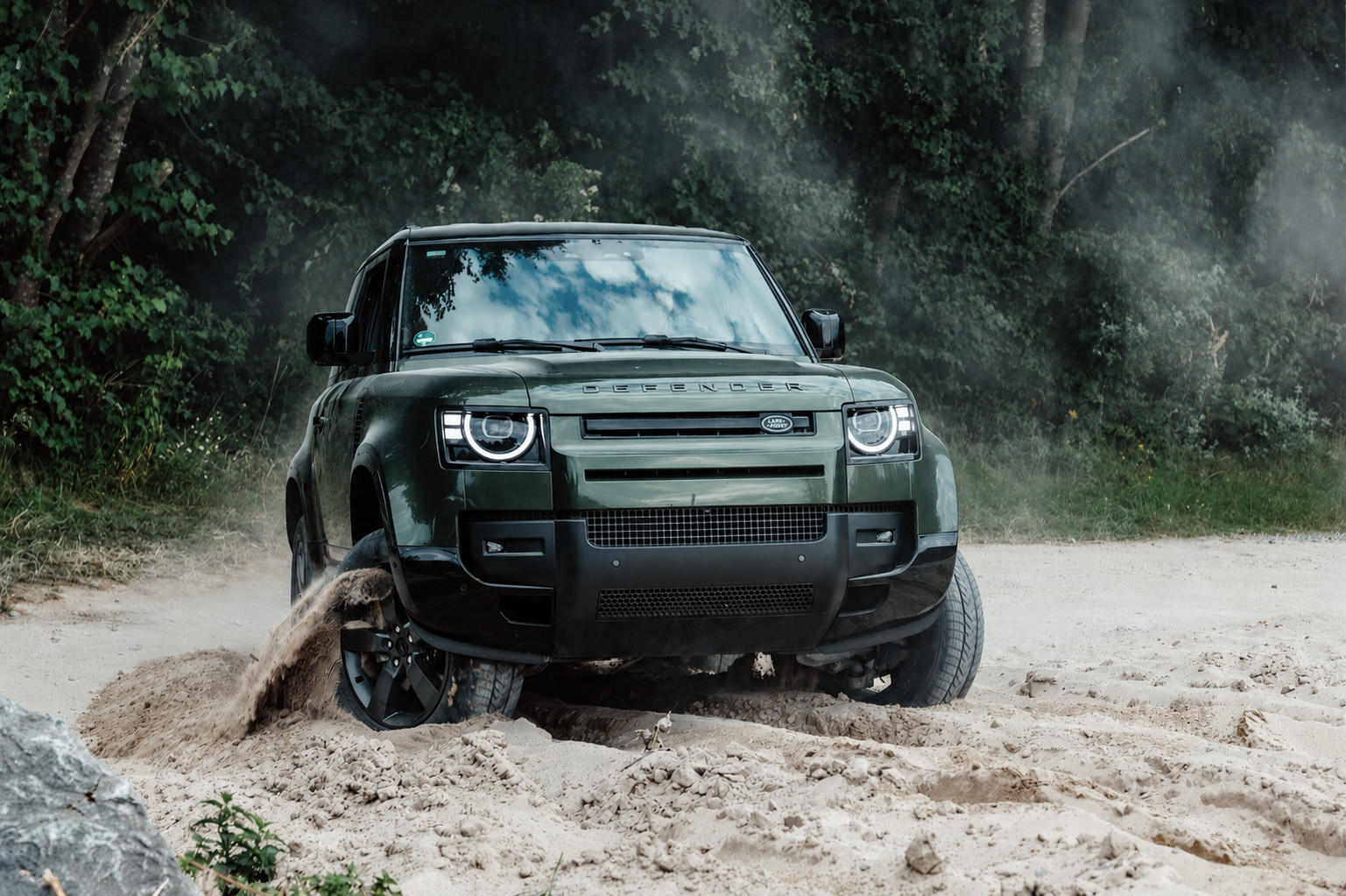 Grüner Defender 110 auf sandiger Offroad-Piste am Waldrand